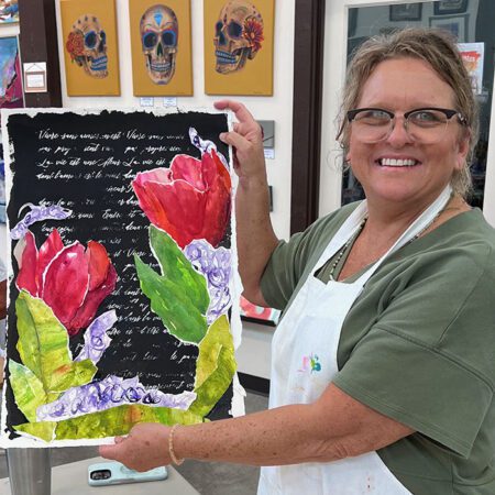 Woman smiling and holding up her painting of roses and a poem.