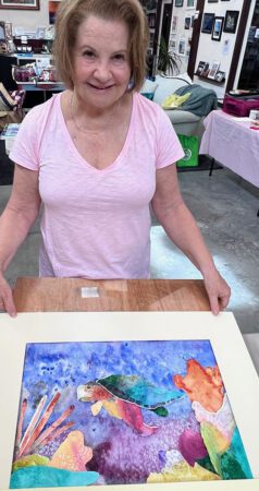 Woman holding her watercolor painting of a turtle.
